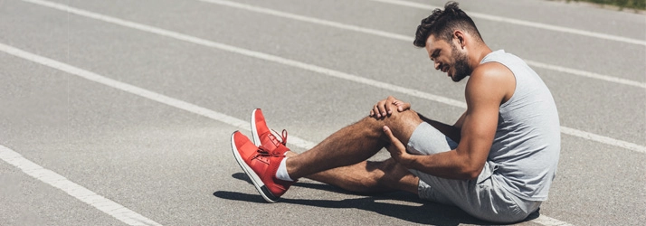 Chiropractic Gilbert AZ Knee Pain Track Runner Injury A runner holding his knee in pain while sitting on a track.