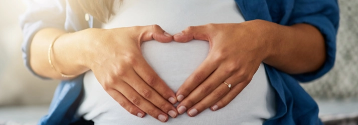 Pregnant woman holding her hands in a heart shape on her belly.
