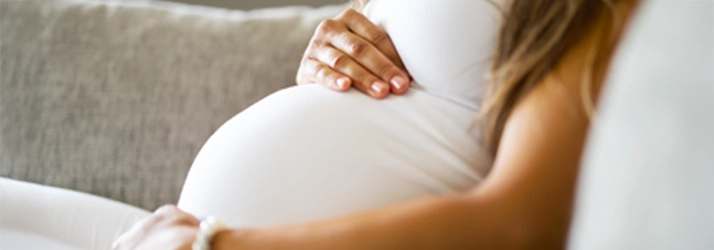 Chiropractic Gilbert AZ Pregnant Woman A pregnant woman holding her round belly while sitting on a couch.